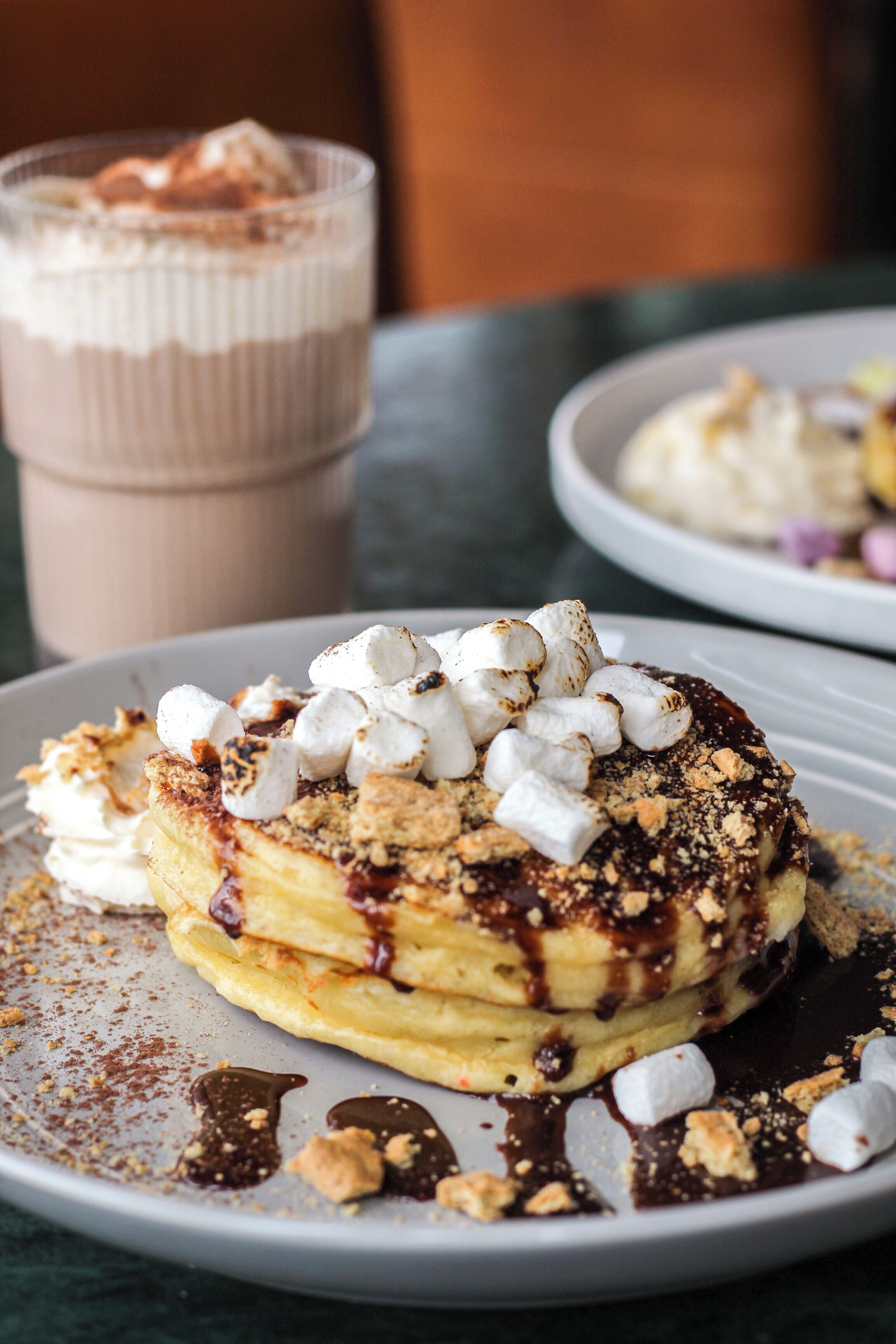 A dessert plate with pancakes topped with marshmallows, chocolate sauce, and crumbled cookies.