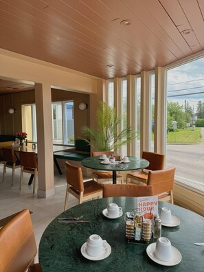 A dining area with a round table set for four, surrounded by chairs. There is a plant in the center, and the table has a sign that reads "HAPPY HOUR". - Auberge Le Parasol  (Saguenay)