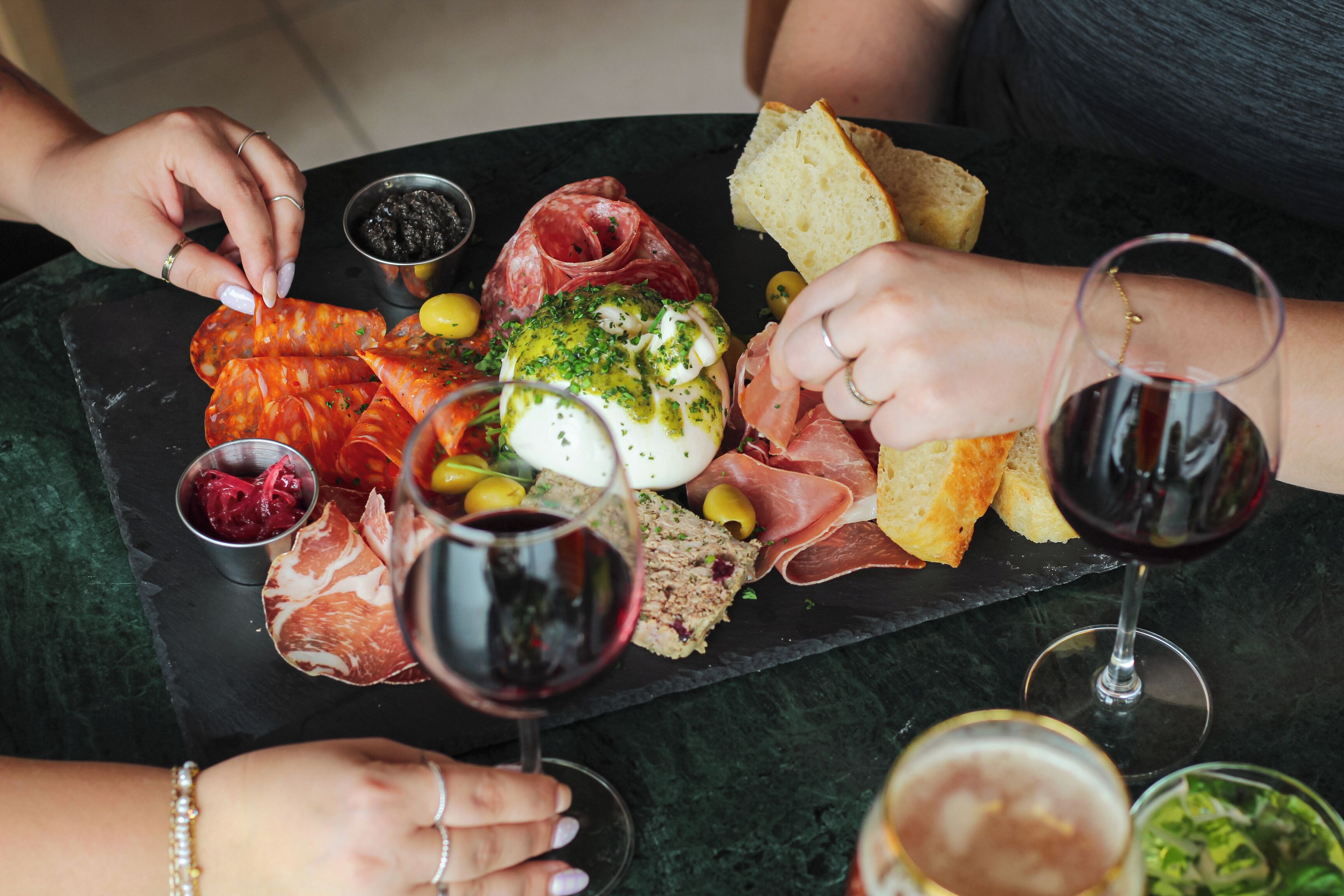 Una tabla de pizarra negra con diversos alimentos y copas de vino.