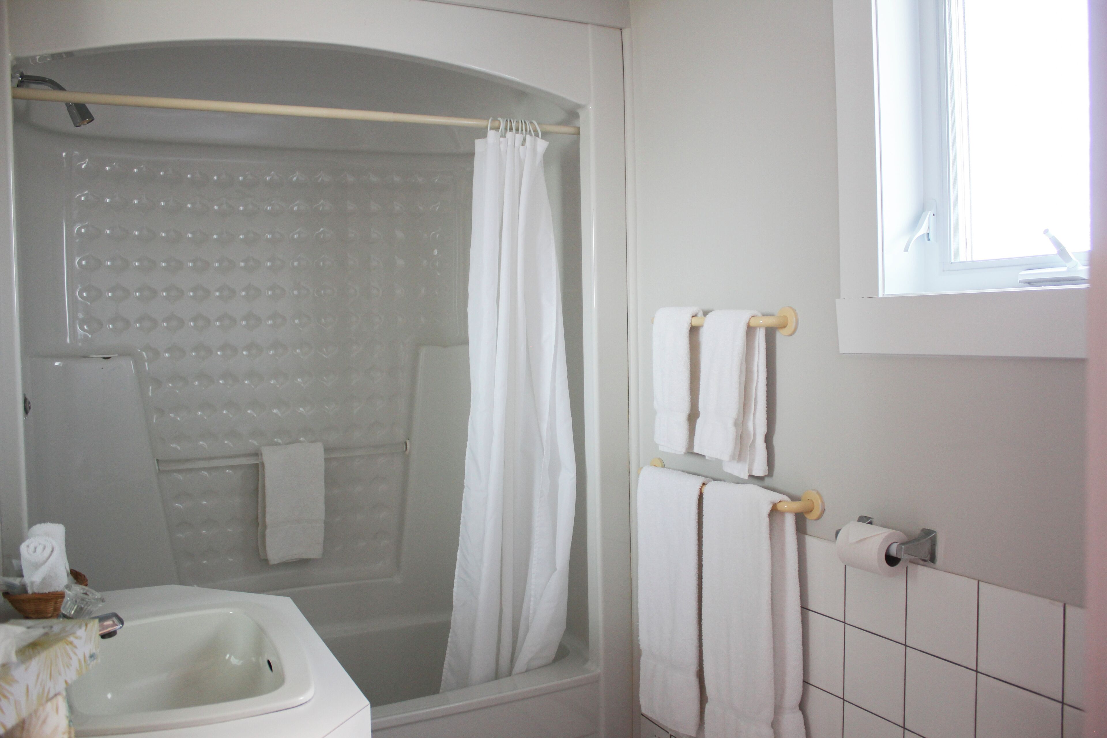 Un baño con bañera, ducha e inodoro. Hay toallas colgadas en la pared y una ventana que proporciona luz natural.