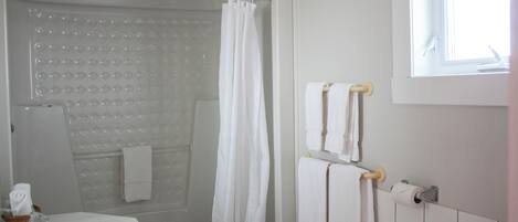Un baño con bañera, ducha e inodoro. Hay toallas colgadas en la pared y una ventana que proporciona luz natural.