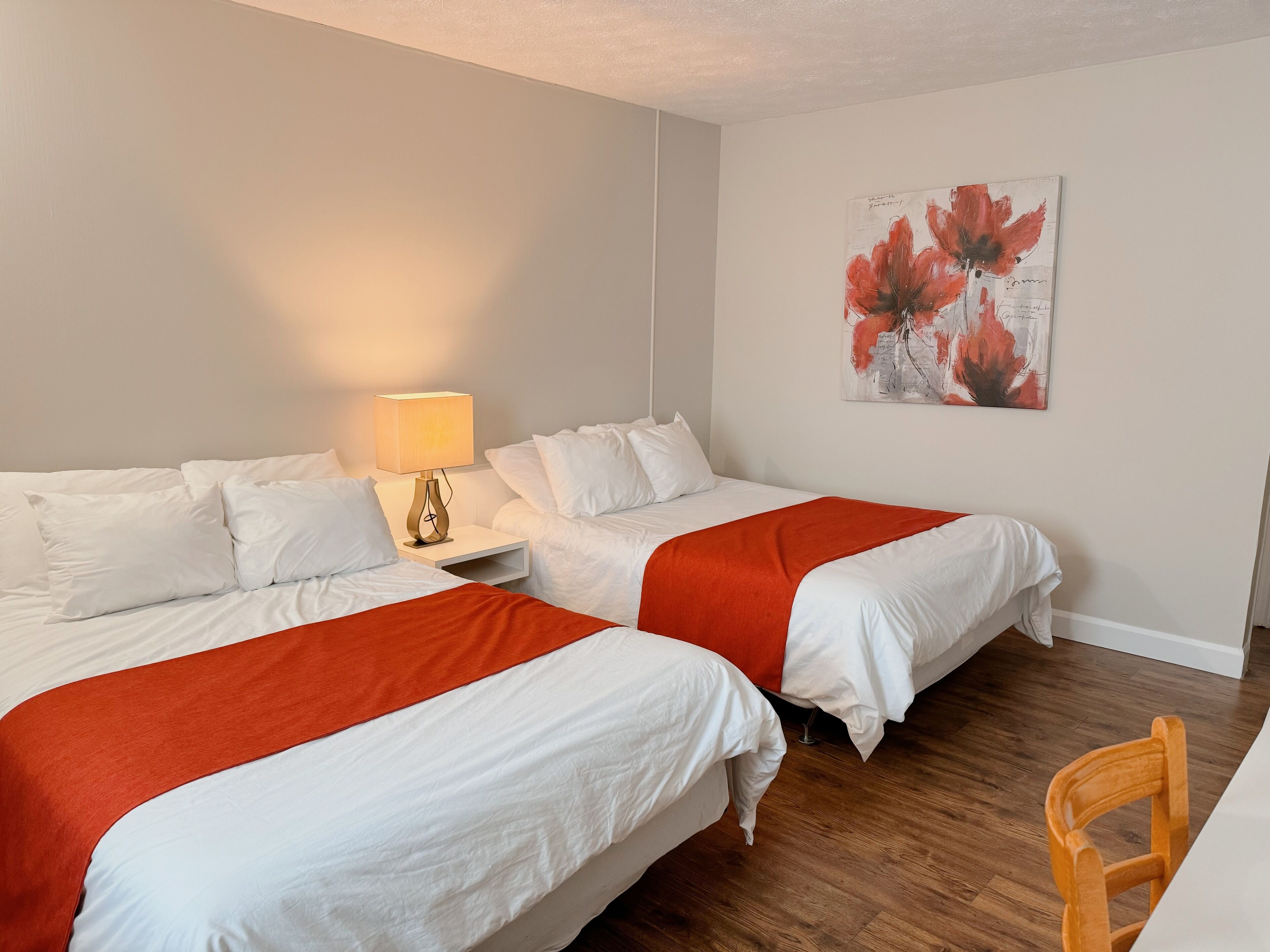 Ein Hotelzimmer mit zwei Betten, einem Nachttisch mit Lampe, Holzboden und einem Bild an der Wand.
