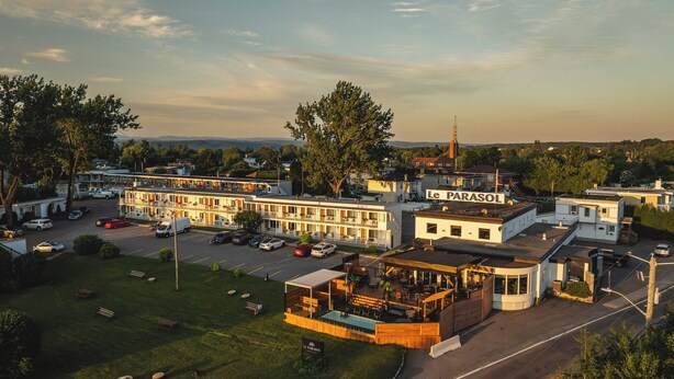 Un motel con varias edificaciones, una piscina y una iglesia al fondo.