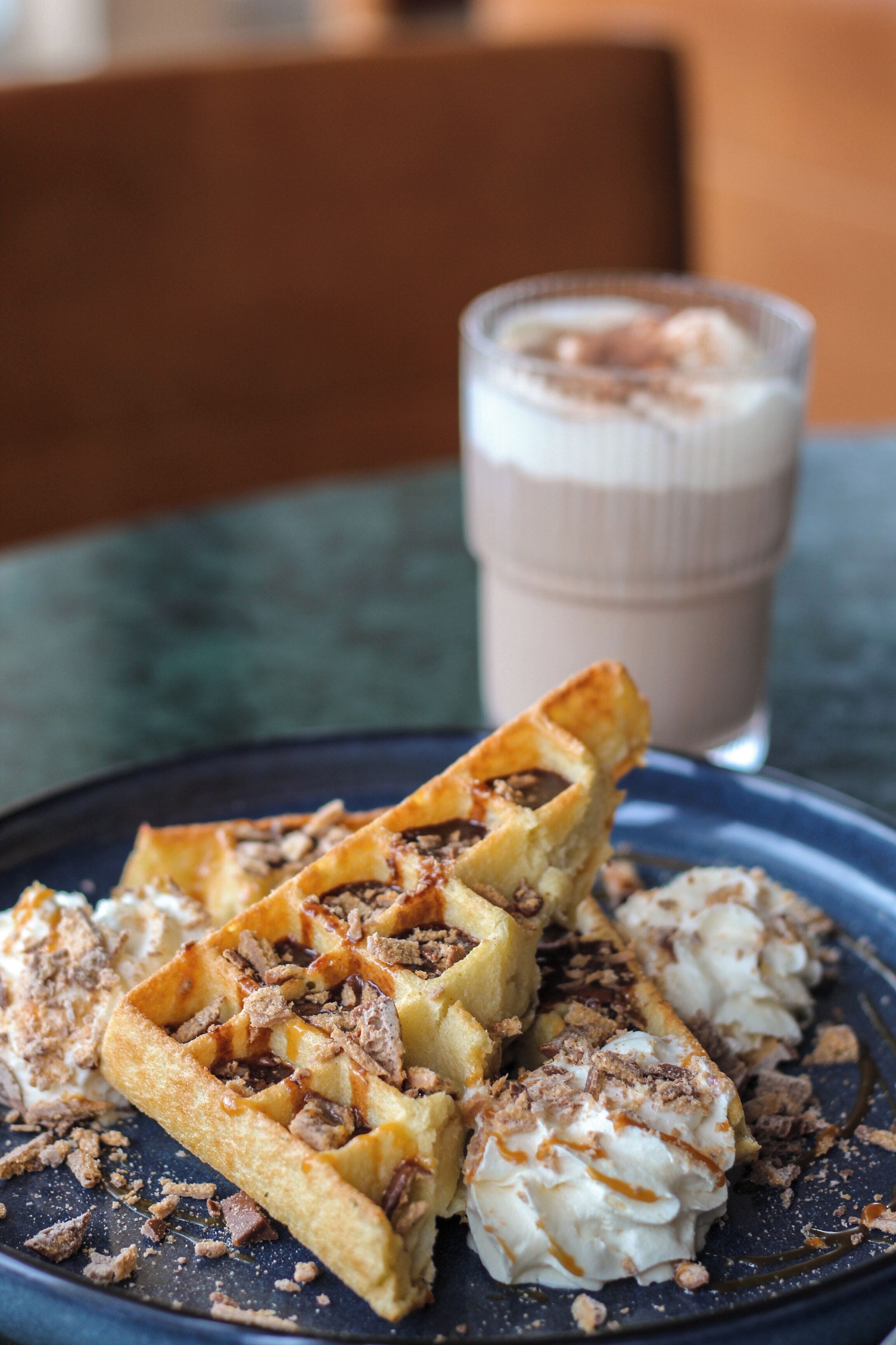 A plate of waffles with toppings and a glass of a creamy beverage on a table.