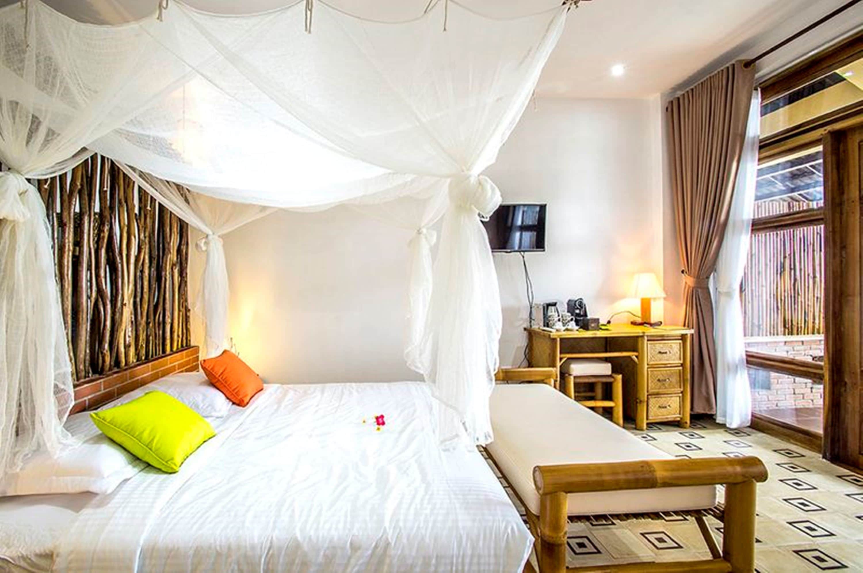 A room with a bed under a canopy, a desk with a chair, a TV, and a window with curtains.