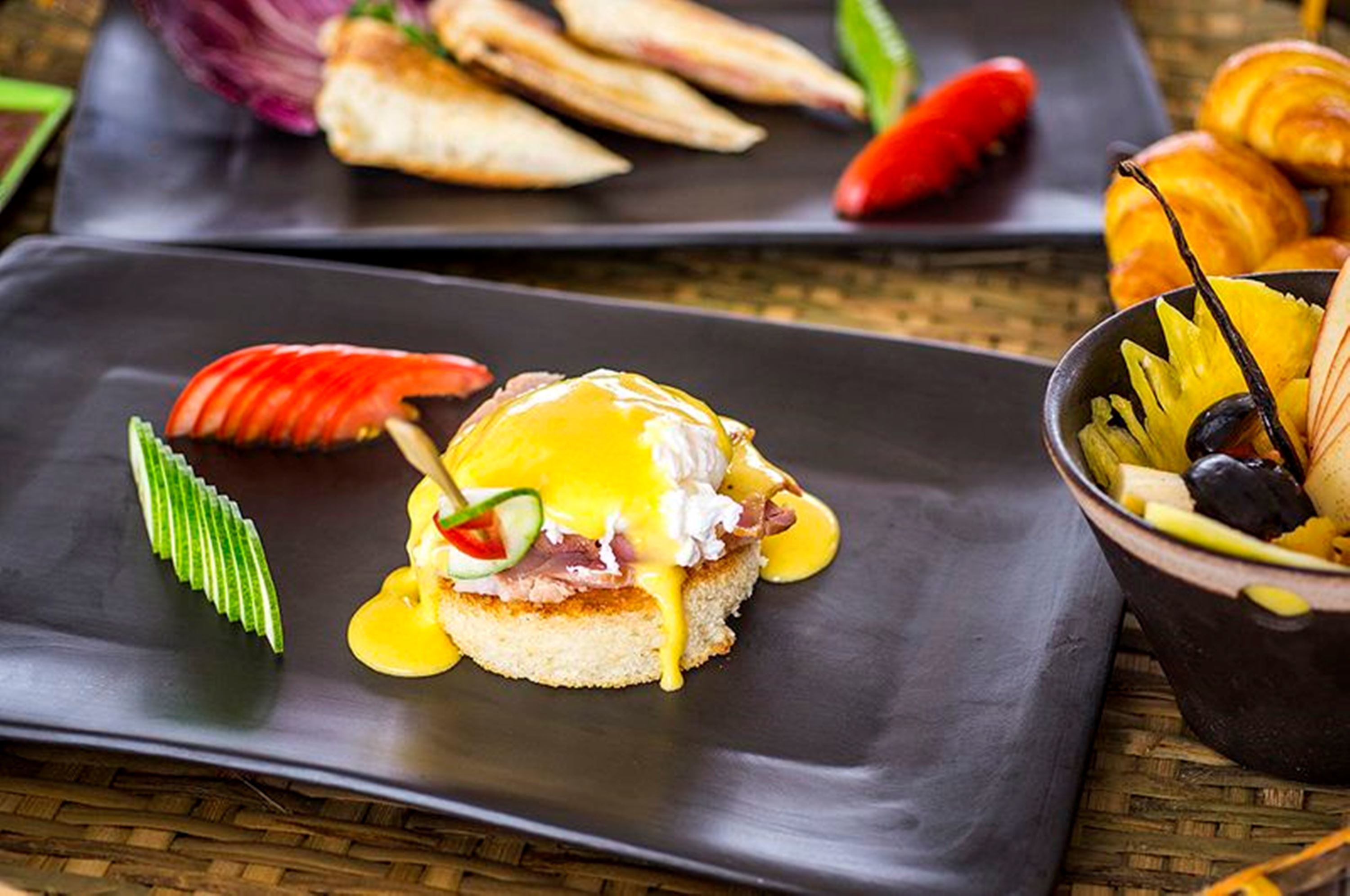 Ein Frühstückstisch mit Eggs Benedict, Croissants und einer Obstschale.