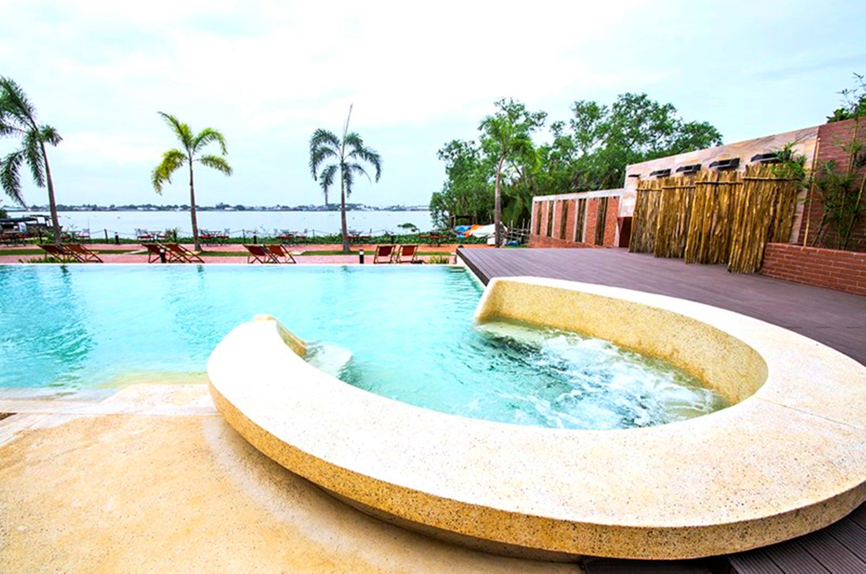 A pool with a hot tub, lounge chairs, and a view of the sea.