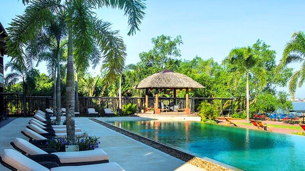 A pool area with lounge chairs, a thatched-roof gazebo, and palm trees. - The Island Lodge (Thoi Son)
