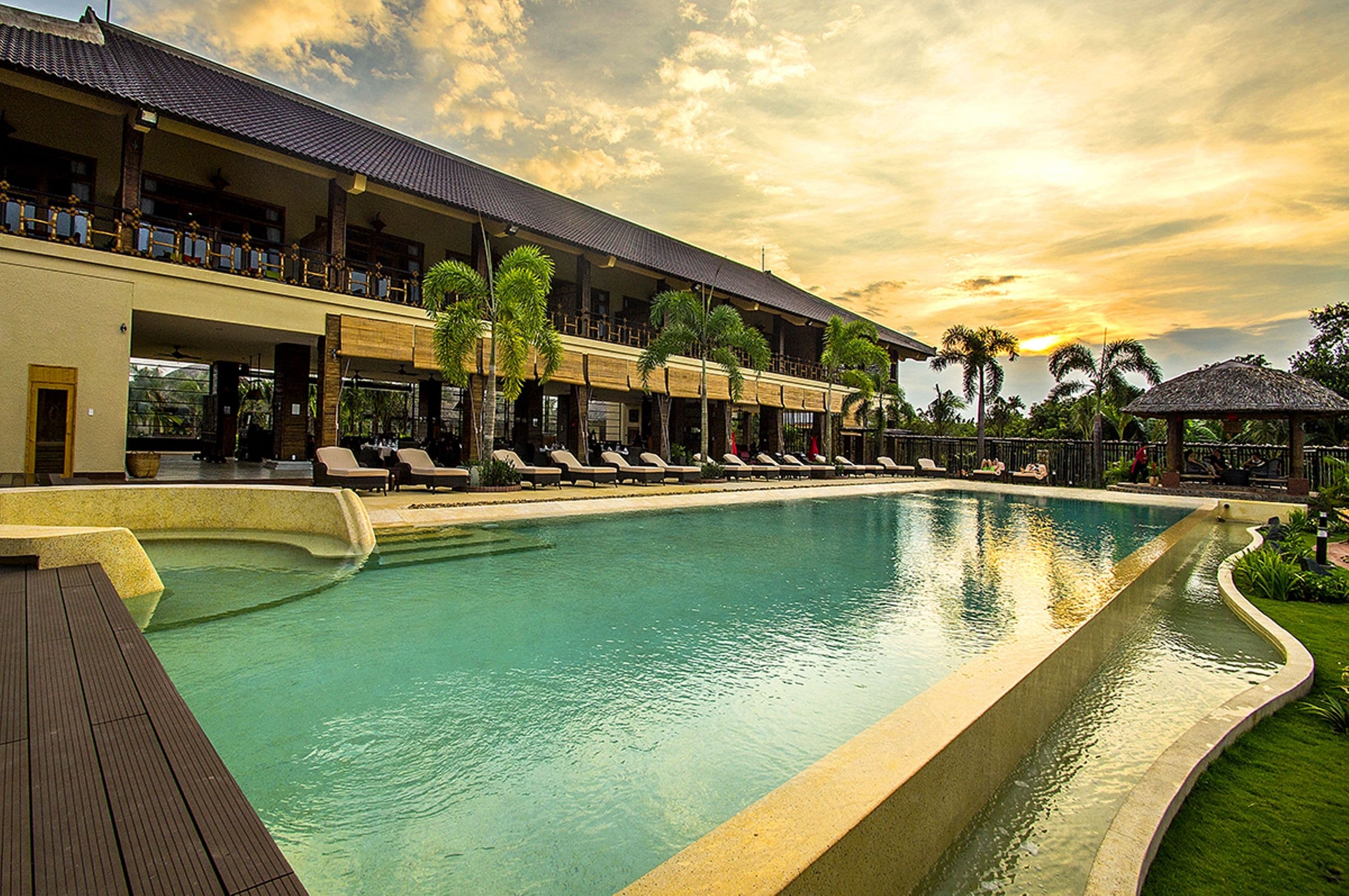 A large outdoor swimming pool with lounge chairs and a building with balconies.