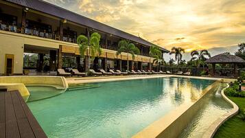 A large outdoor swimming pool with lounge chairs and a building with balconies.
