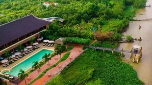 An aerial view of a resort with a swimming pool, lounge chairs, and a dock extending into a river. - The Island Lodge (Thoi Son)