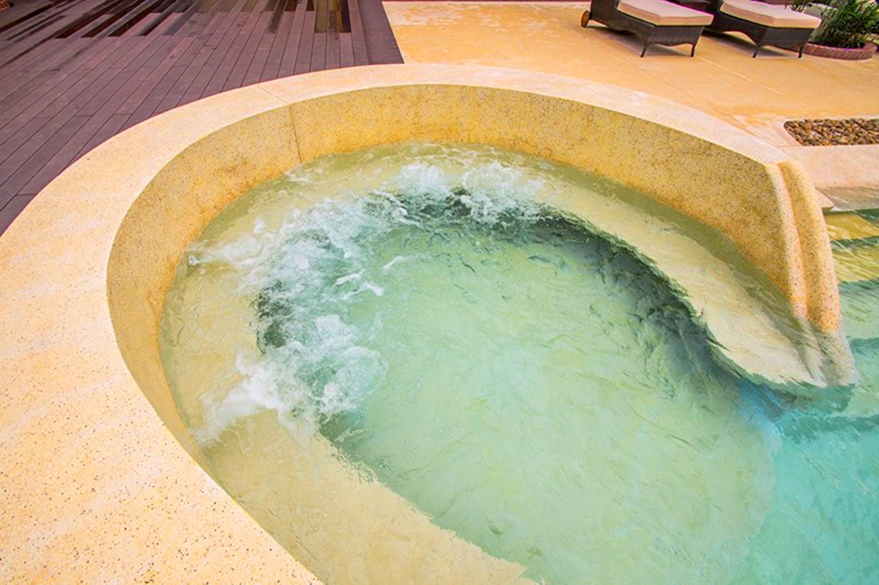 Een hottub met een gebogen rand, omringd door een betegeld terras met loungestoelen.