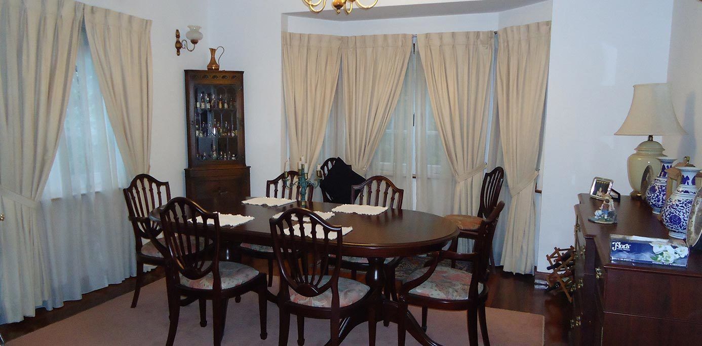 A dining room with a wooden table and chairs, a cabinet with glass doors, and a lamp on a side table.