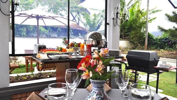 A dining area with a table set for two, a grill, and a view of a body of water and greenery. - Cocoon Hills (Nuwara Eliya)