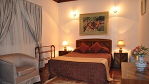 A bedroom with a bed, a chair, two bedside tables with lamps, a painting on the wall, and a vase with flowers on a side table. - Cocoon Hills (Nuwara Eliya)