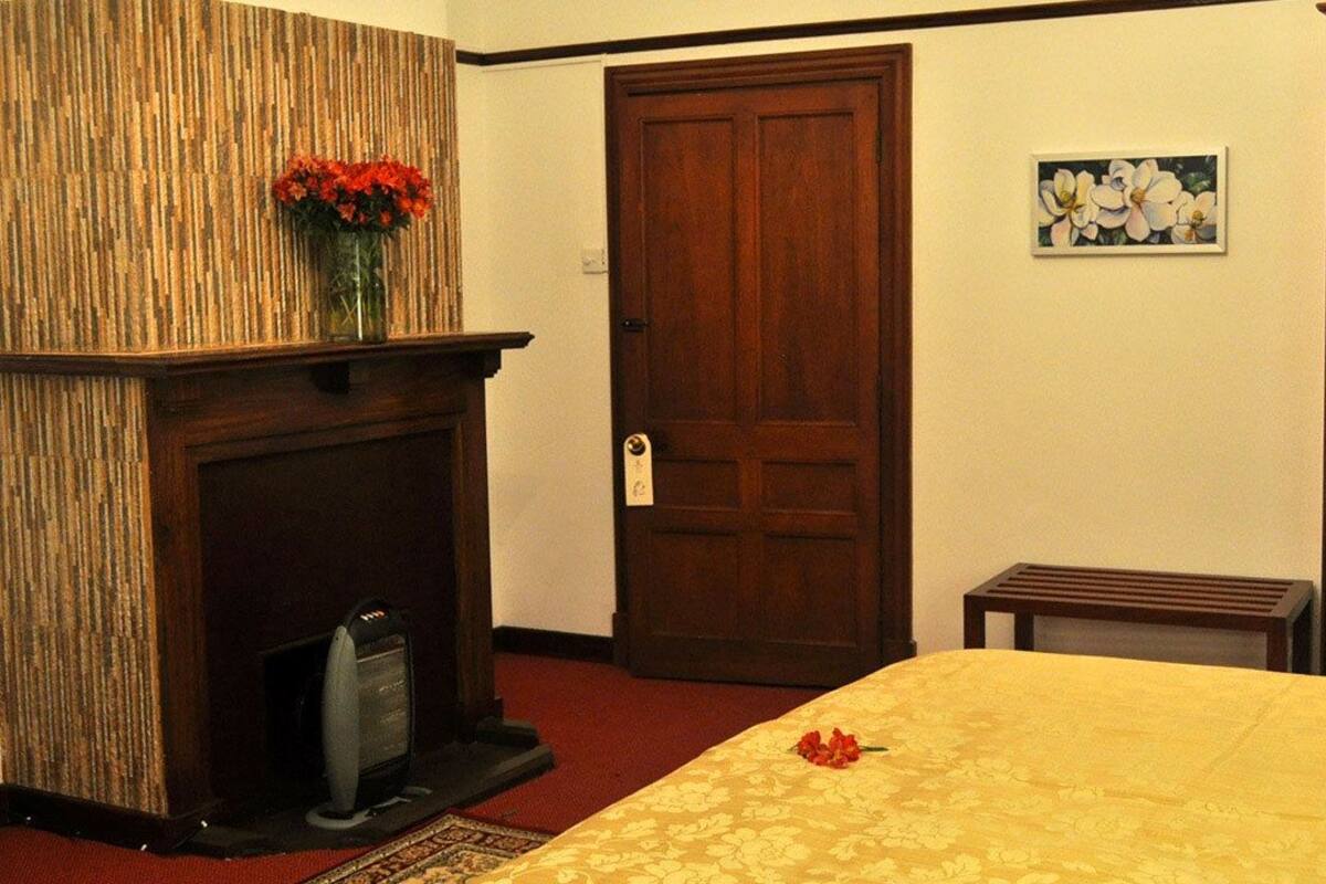 A hotel room with a fireplace, a bed with a yellow bedspread, a wooden door, and a small table.