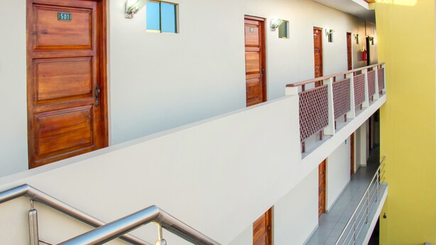 A hotel corridor with wooden doors, a metal railing, and a yellow wall. - Colon Plaza Hotel (Ica)