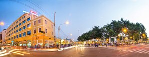 A multi-story hotel with a prominent 'HOTEL' sign, a pedestrian crossing, and a well-lit street with trees and benches. - Colon Plaza Hotel (Ica)