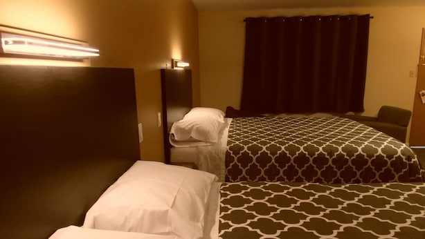 A hotel room with two beds, a dark curtain, and a wall-mounted light fixture. - West View Motel (Hanna)