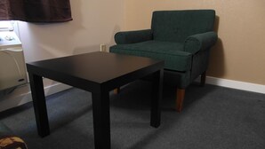 A room with a dark wooden table, a green armchair, and a beige wall. - West View Motel (Hanna)