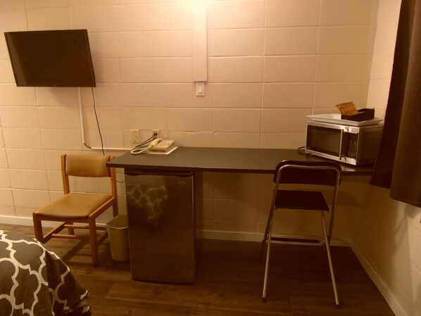 A compact kitchenette with a refrigerator, microwave, and a small table with a telephone. - West View Motel (Hanna)