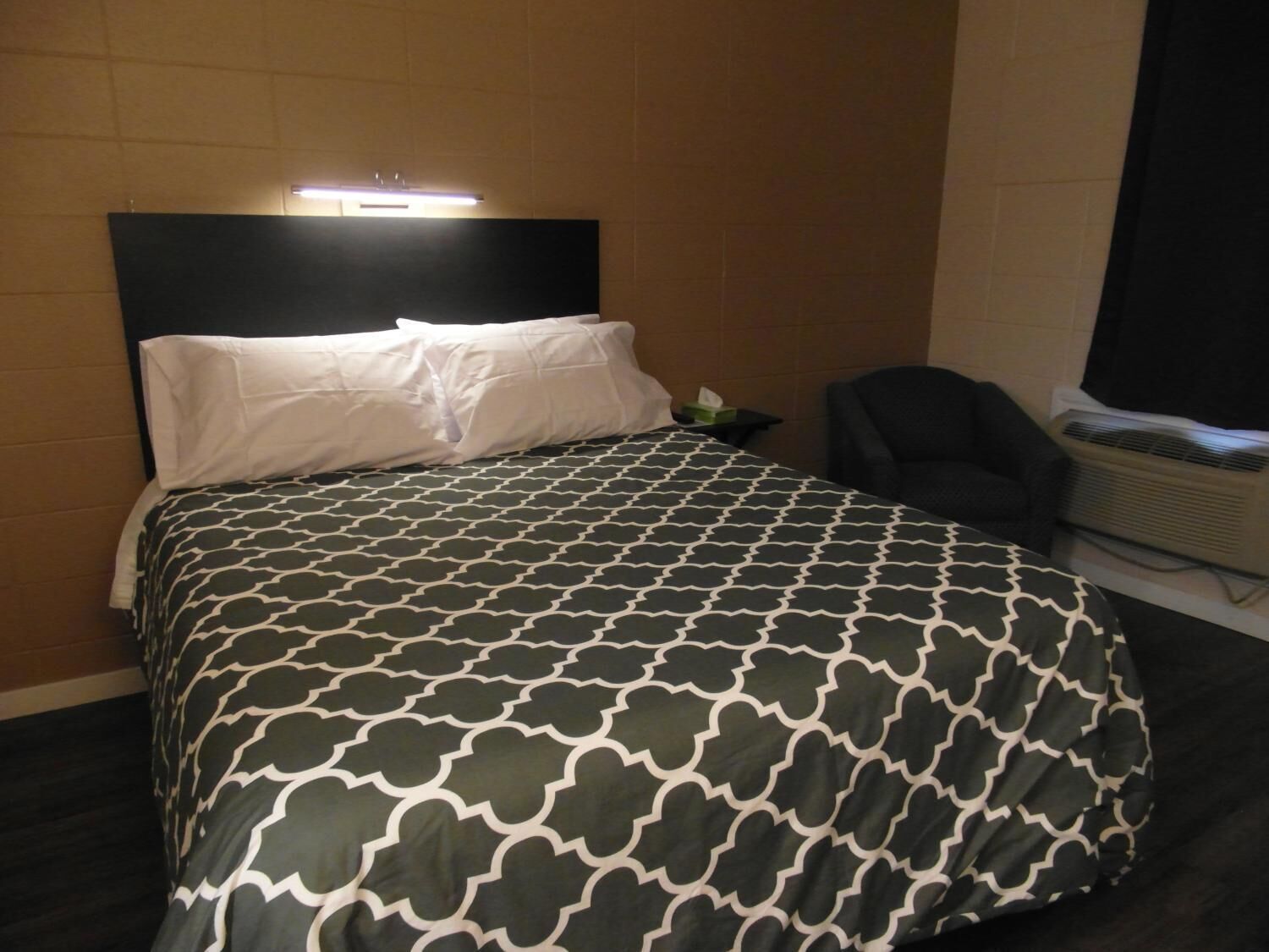 A hotel room with a bed, a chair, and an air conditioning unit.