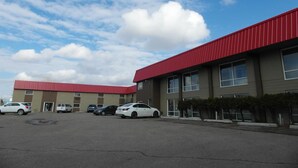 A parking lot with several cars and a building with a red roof and multiple windows. - West View Motel (Hanna)