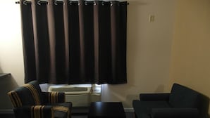A hotel room with a bed, two armchairs, a small table, and a window with curtains. - West View Motel (Hanna)
