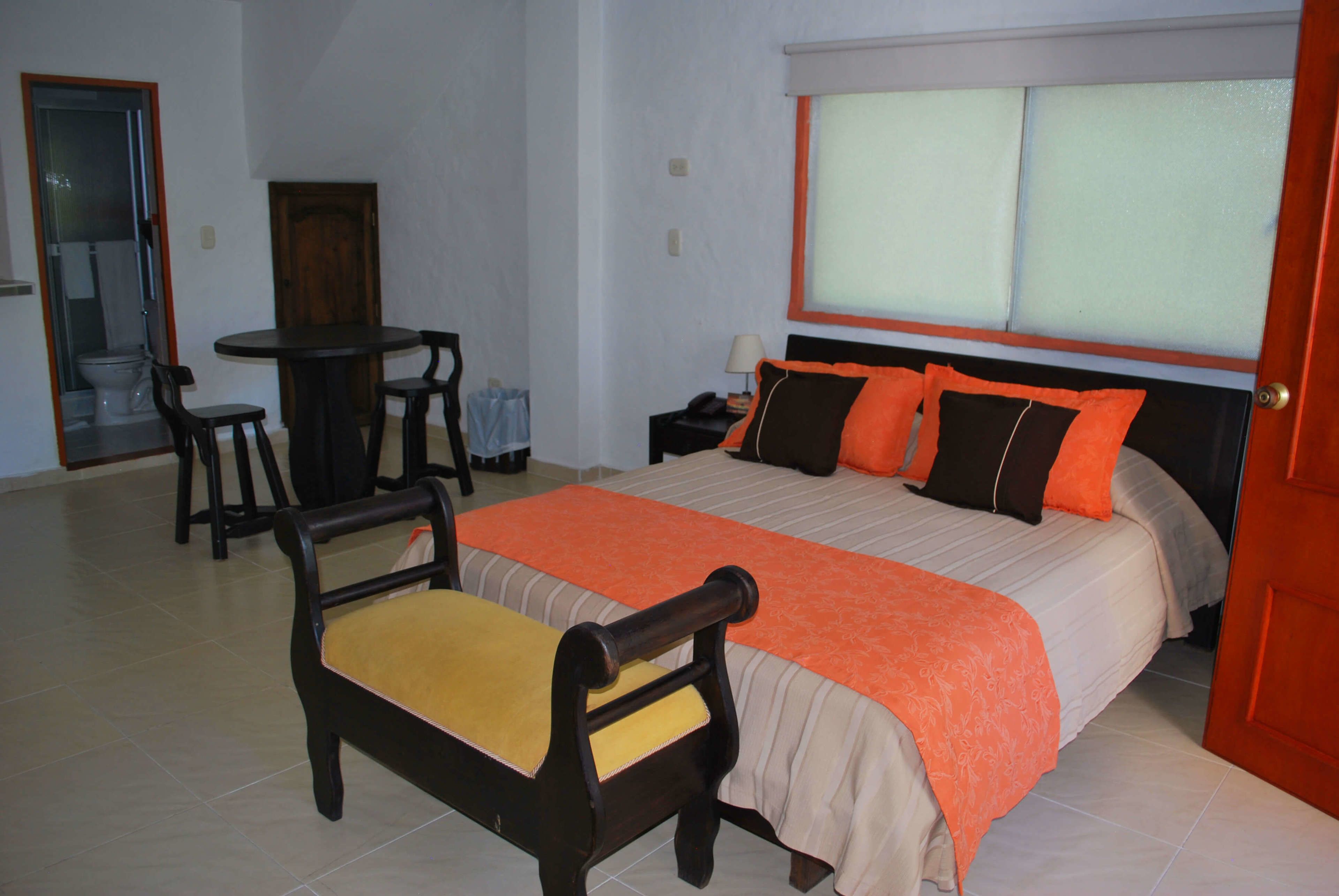 Una habitación de hotel con cama, una silla, una mesa y un baño visible a través de una puerta abierta.