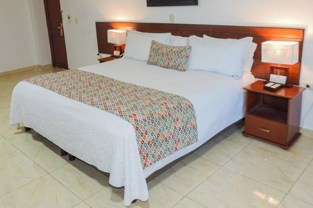A hotel room with a large bed, two bedside tables with lamps, a wooden headboard, and a framed picture on the wall.