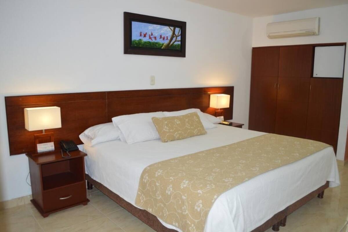 A hotel room with a large bed, two bedside lamps, a nightstand with a phone, a wardrobe, and a framed picture on the wall.