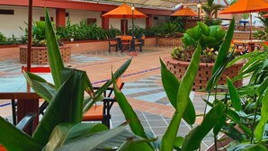 An outdoor patio area with orange umbrellas, tiled flooring, and potted plants. - Hotel Hacaritama Colonial (Villavicencio)