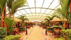 A covered walkway with tables and chairs, surrounded by greenery and palm trees. - Hotel Hacaritama Colonial (Villavicencio)