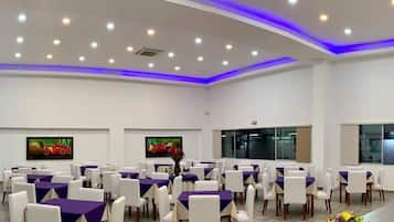 Une salle de conférence aux murs blancs, avec des nappes violettes et des chaises blanches.