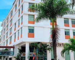 A multi-story hotel with a white facade and orange accents, featuring a palm tree in the foreground.
