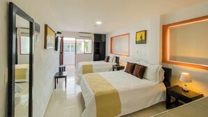 A hotel room with two beds, a large mirror, a bedside table with a lamp, and a painting on the wall. - Hotel Hacaritama Colonial (Villavicencio)