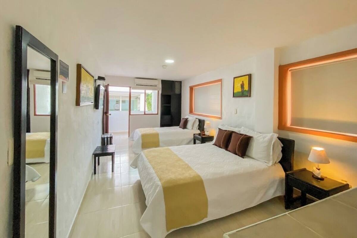 A hotel room with two beds, a large mirror, a bedside table with a lamp, and a painting on the wall.