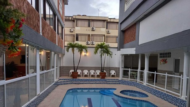 A swimming pool with a tiled edge, surrounded by a low brick wall and a white fence. - Hotel Napolitano (Villavicencio)