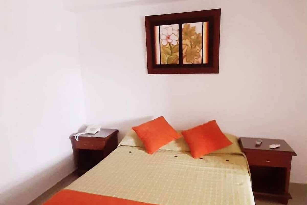 Ein Einzelbett mit gestreifter Bettdecke, zwei Nachttische und ein kleines Fenster mit floralem Dekor.