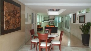 A hotel lobby with a dining area featuring a round table and four chairs, a large wooden sculpture on the wall, and a staircase leading to an upper level. - Hotel Napolitano (Villavicencio)