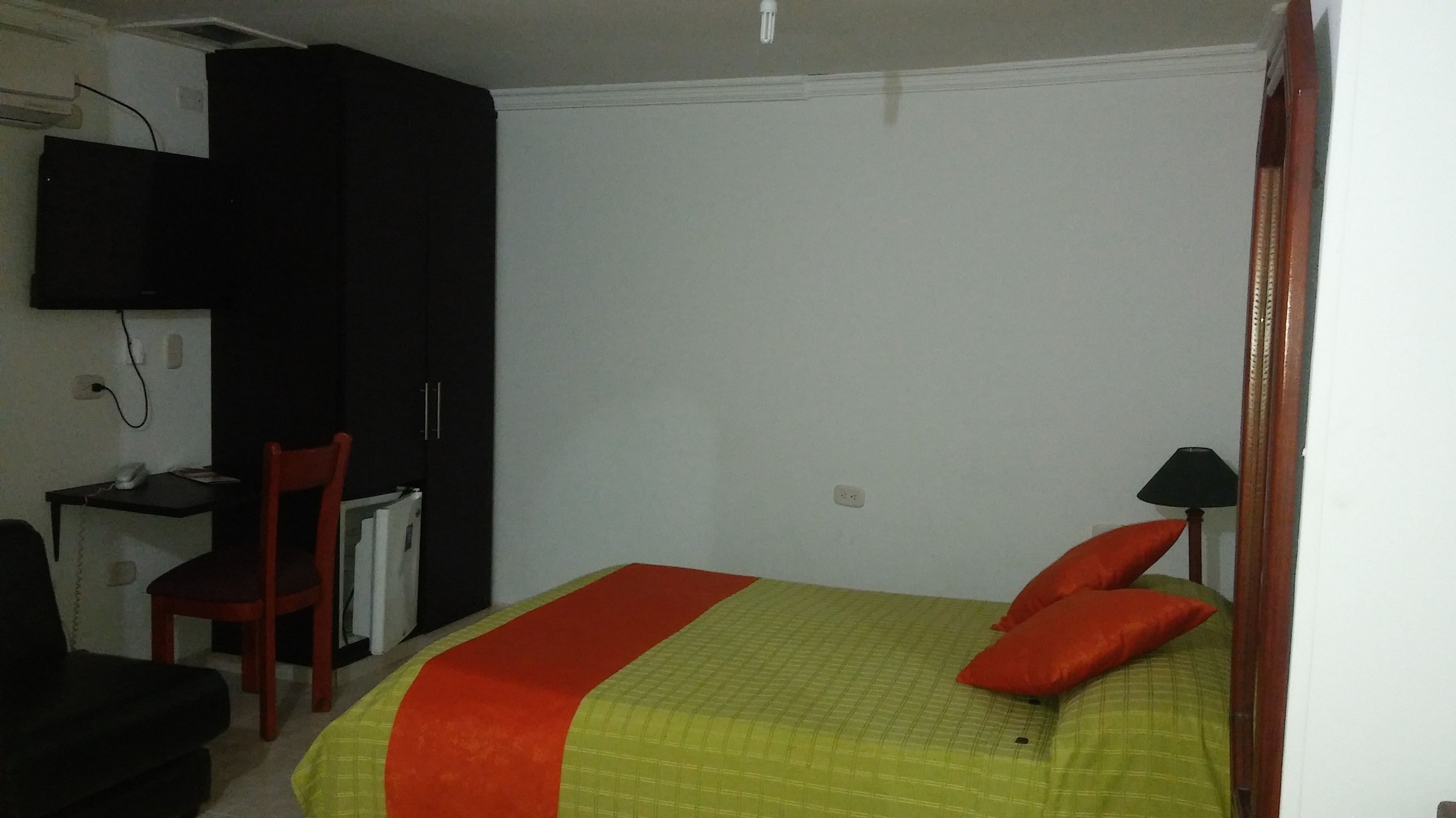 Un dormitorio con cama, escritorio, silla, armario y televisión.