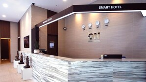 Zona d'entrada d'un hotel modern, amb un taulell de marbre, rellotges i un cartell que diu "SMART HOTEL".