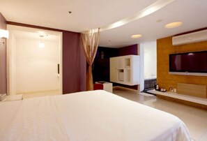 Una habitación de hotel moderna con una cama grande, televisión montada en la pared y un minibar.