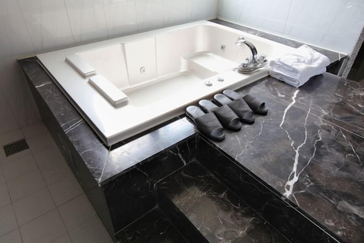 A modern bathroom with a large bathtub, a vanity with a mirror, and a set of black towels on the counter.