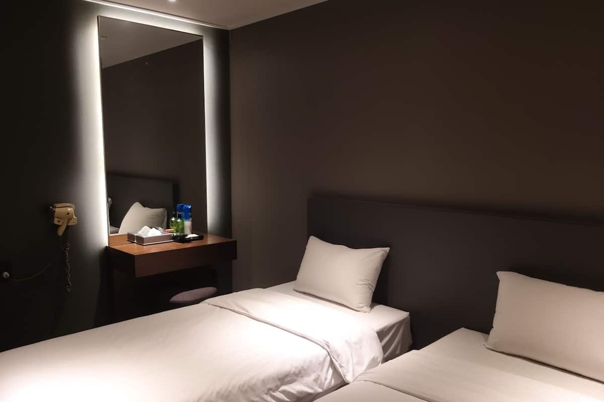 Hotellihuone, jossa on kaksi erillistä sänkyä, yöpöytä lampun kanssa, peili ja puhelin.