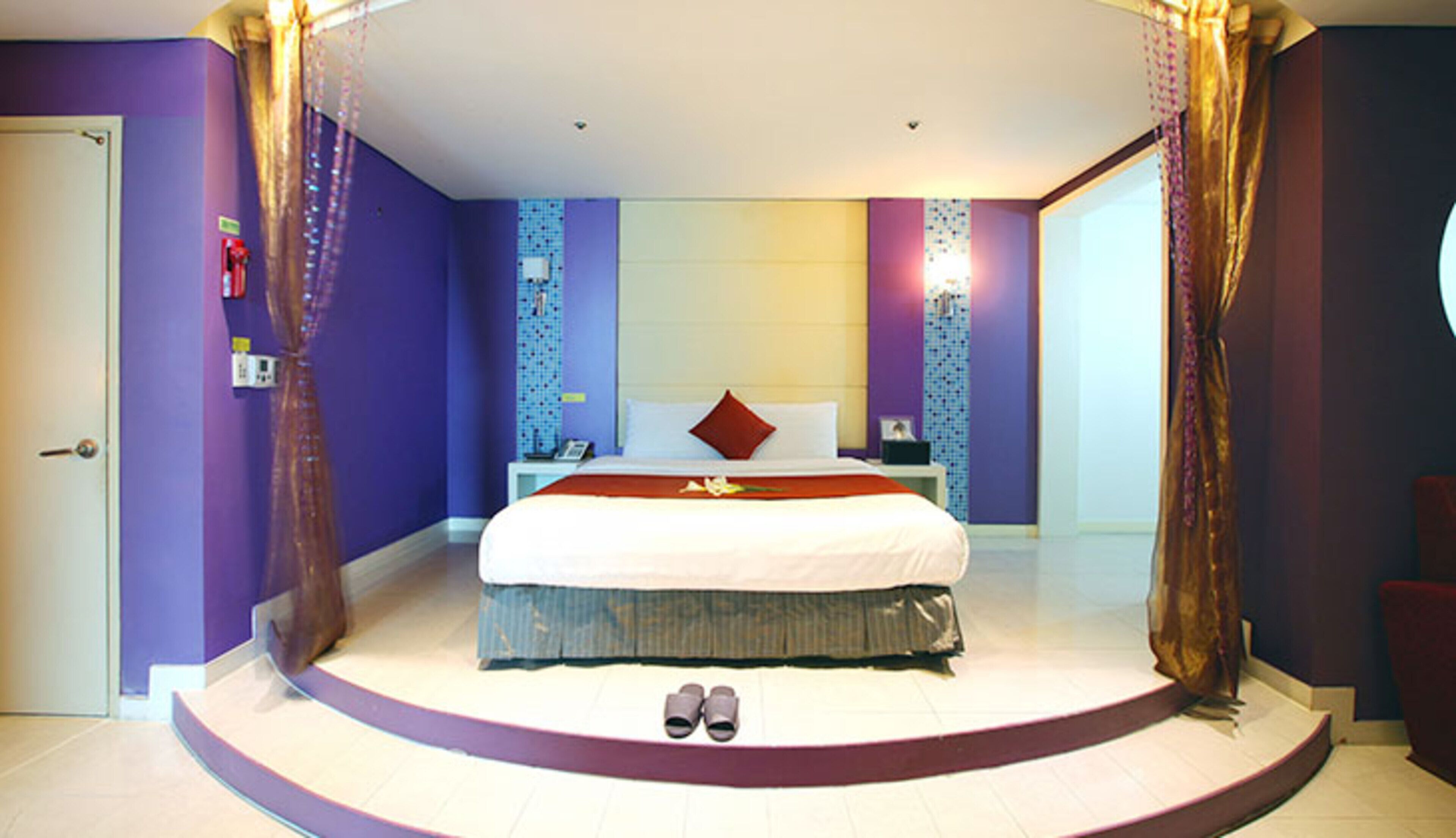 A bedroom with a large bed, a nightstand, a dresser, and a door.