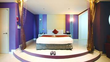 A bedroom with a large bed, a nightstand, a dresser, and a door.