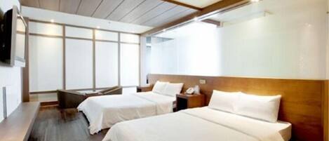 A hotel room with two beds, wooden headboards, a bench, and a large window.