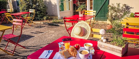 An outdoor dining area with red tables and chairs, a basket of bread, a croissant, a bowl of soup, and a glass of orange juice.