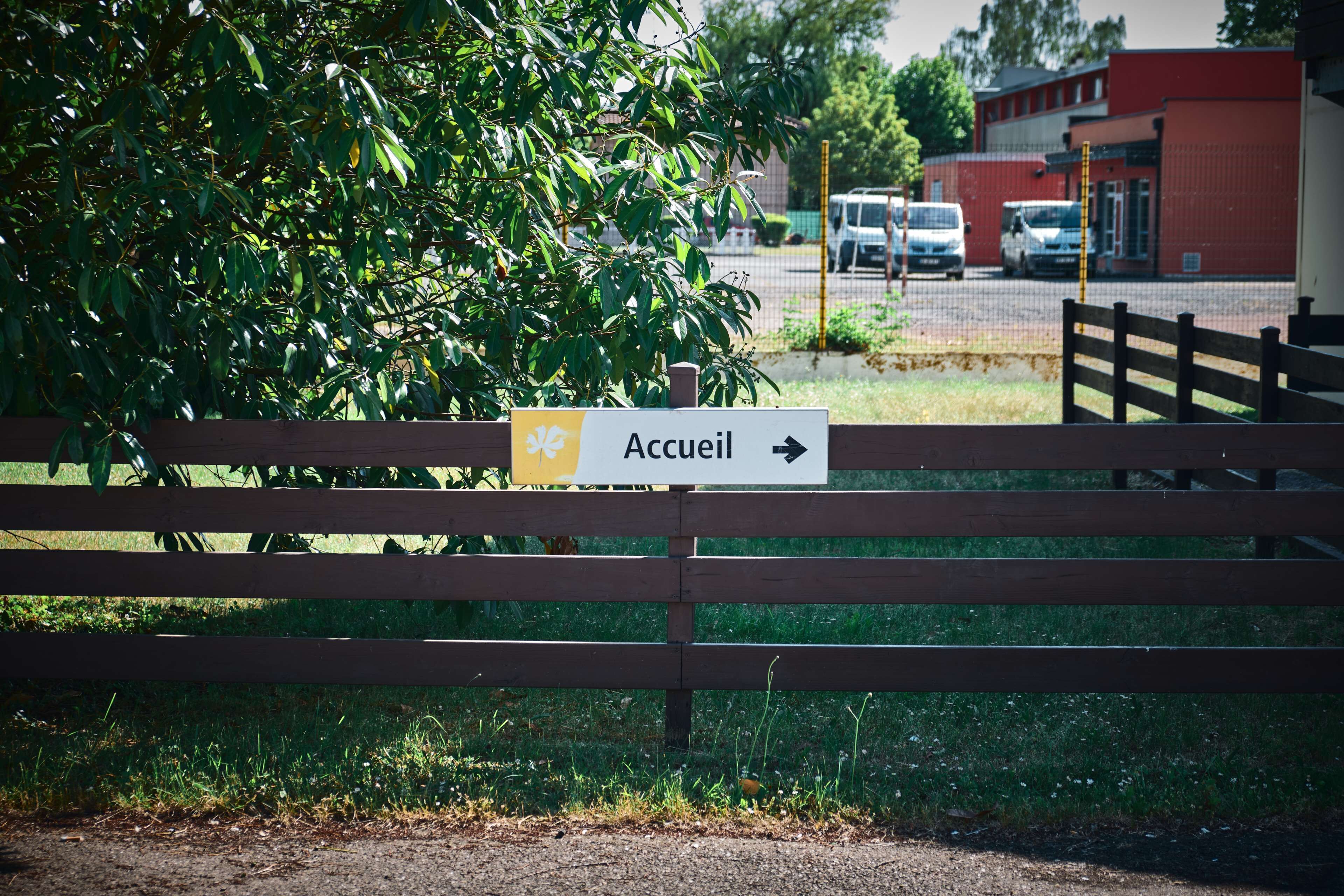 A wooden fence with a sign that reads "Accueil" and an arrow pointing to the right.